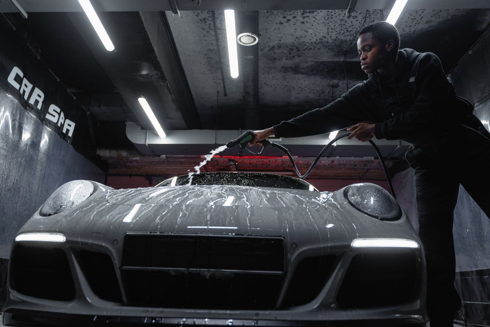 WashBox-style crew member hand cleaning a white sports car indoors